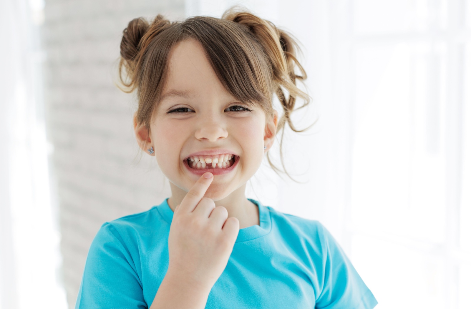 A child proudly smiles and points at the gap where their front bottom tooth used to be.