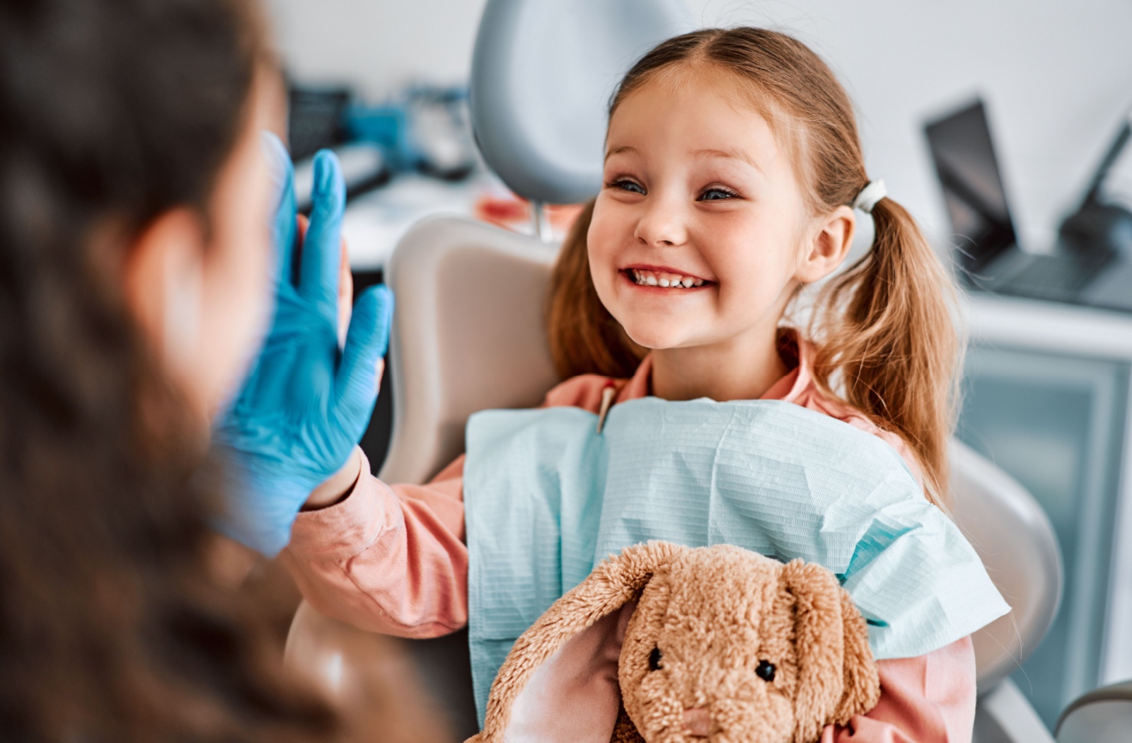 A smiling child high-fives their dentist after a successful oral health exam.