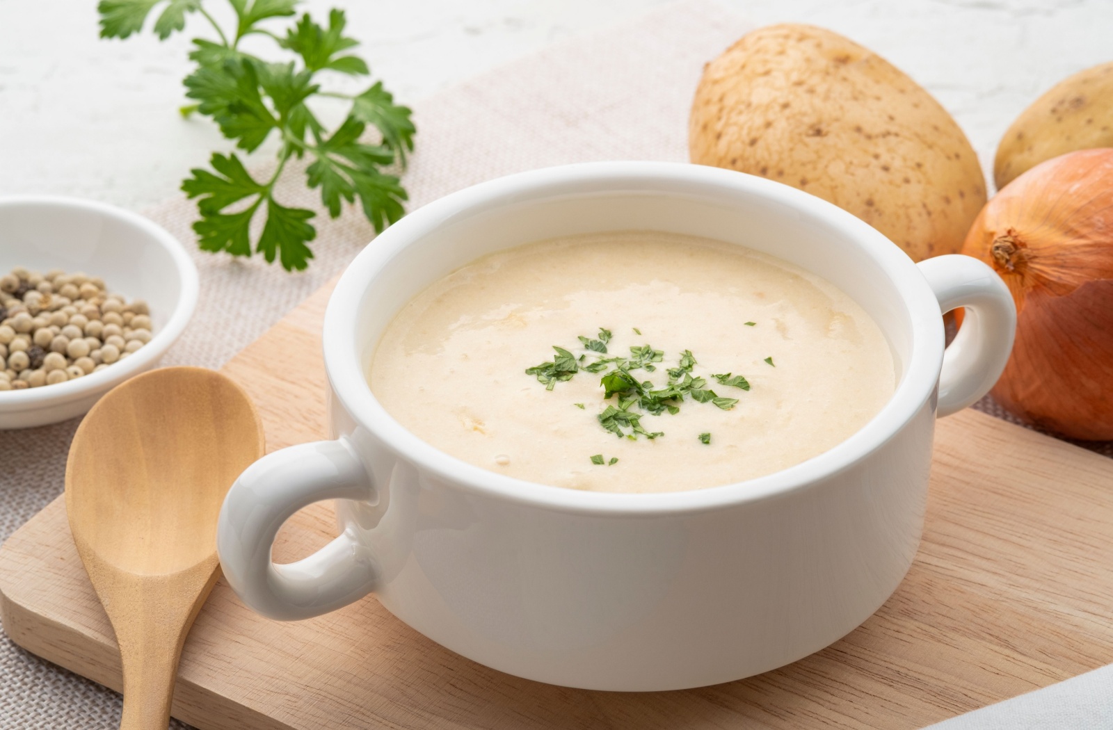 a bowl of warm potato soup with parsley as garnish is on a wooden plate