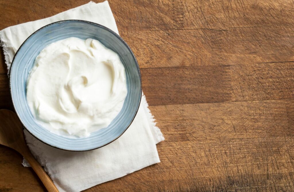 Bird's eye view photo of a bowl of homemade Greek yogurt on top of a wooden table.