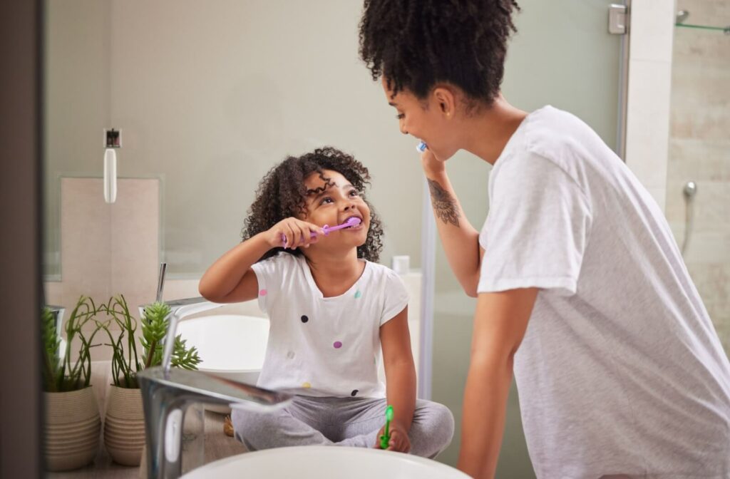 A parent and child brush their teeth together in the morning.