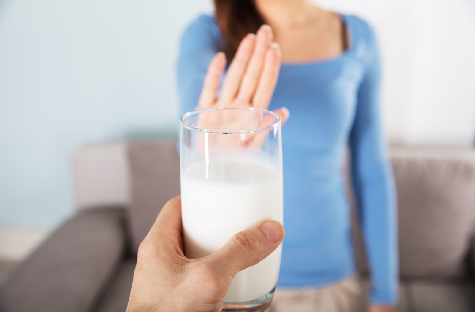 Close-up of a person handing a glass of milk to another person in the background who is holding up a hand to signal they don't want it.